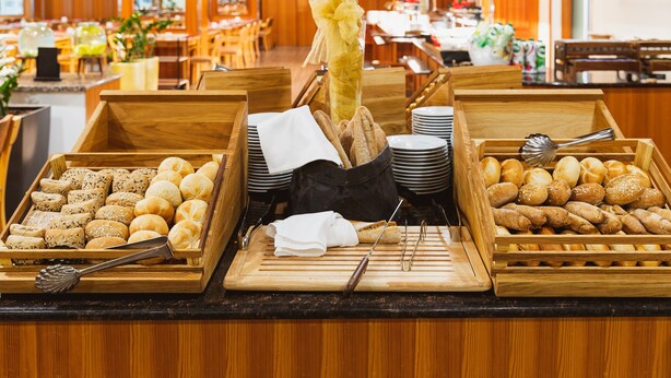 A buffet with various breads and pastries, wooden serving boards, and a decorative vase with dried plants.