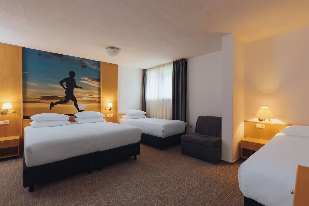 Habitación de hotel con dos camas, un escritorio, una silla y un cuadro de un corredor en la pared.
