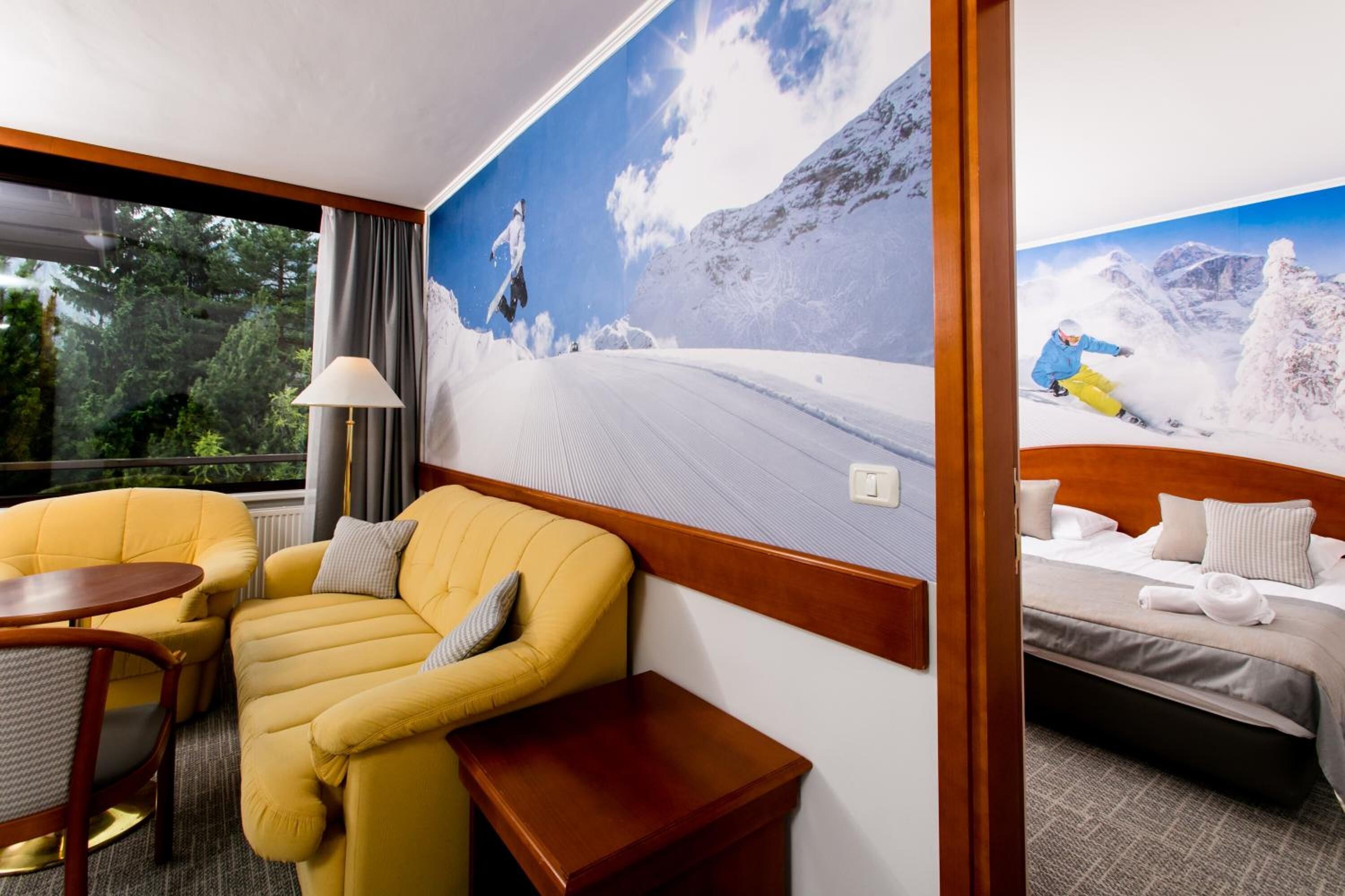 Una camera d'albergo con un letto, una poltrona gialla, un tavolino e un'ampia finestra.