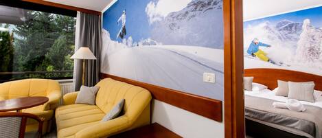 Una camera d'albergo con un letto, una poltrona gialla, un tavolino e un'ampia finestra.