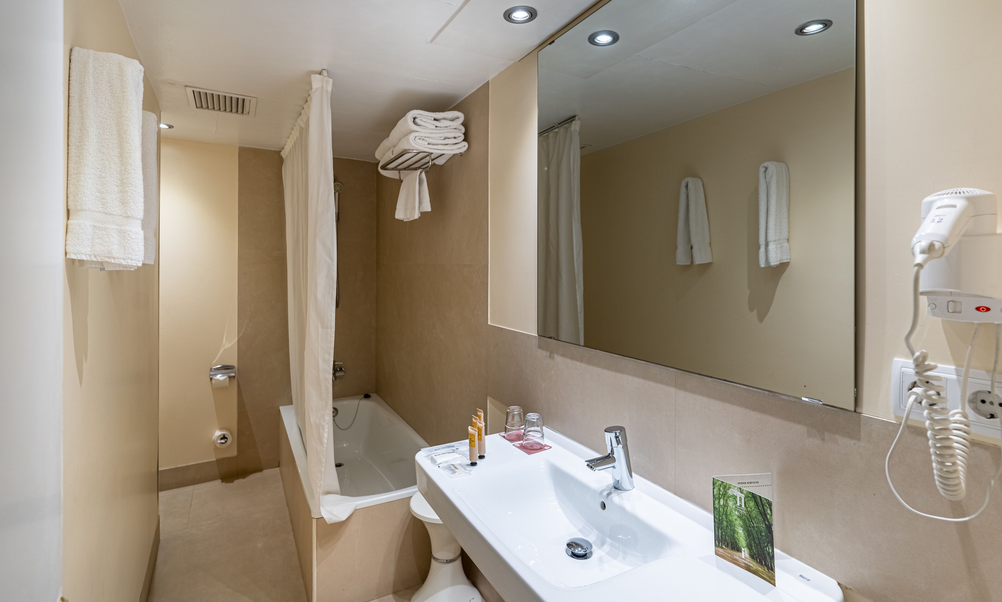 Un baño moderno con lavamanos, espejo y ducha. Hay toallas colgadas en la pared y un secador de pelo sobre el mostrador.