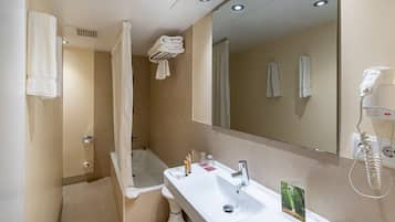Un baño moderno con lavamanos, espejo y ducha. Hay toallas colgadas en la pared y un secador de pelo sobre el mostrador.