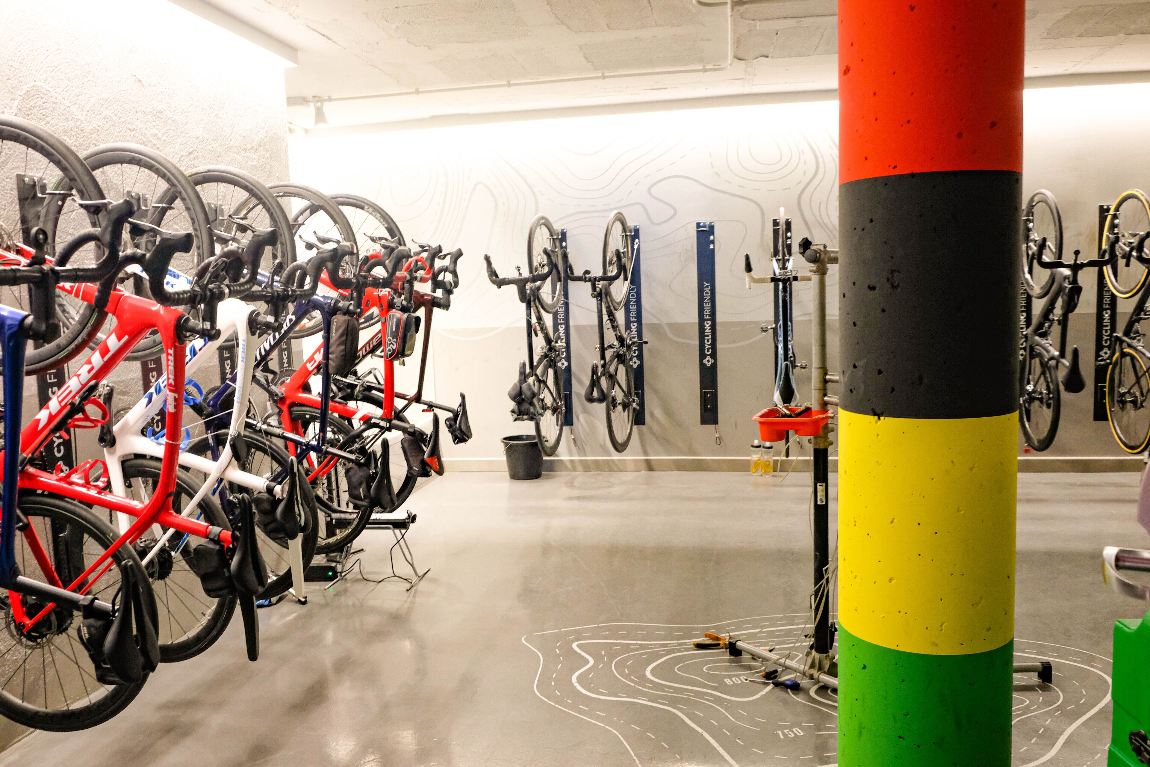 Un aparcamiento para bicicletas con varias bicicletas, un poste rojo, amarillo y verde, y una pared con un diseño peculiar.