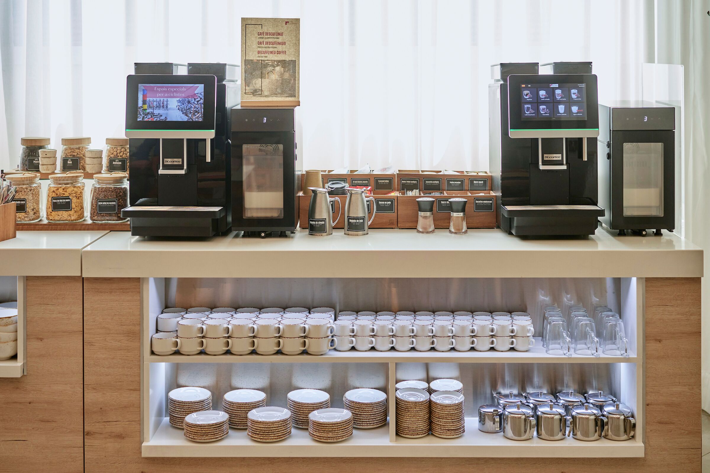 Mostrador de cafetería con dos máquinas de café, una variedad de granos y tazas y platos ordenados.
