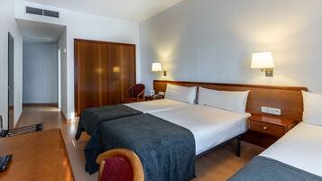 Ein Hotelzimmer mit zwei Betten, einem Schreibtisch mit Stuhl, einem Kleiderschrank und einem Nachttisch mit Lampe.