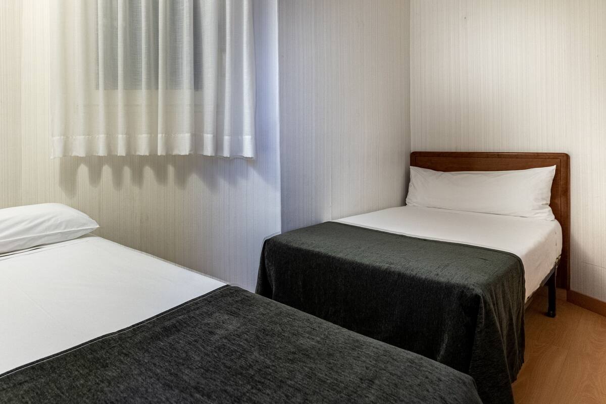 A room with two single beds, each with a wooden headboard and a dark grey bedspread.