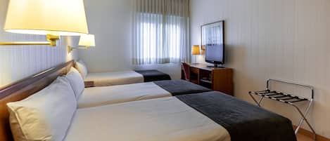Habitación de hotel con dos camas, televisor, escritorio y ventana con cortinas.
