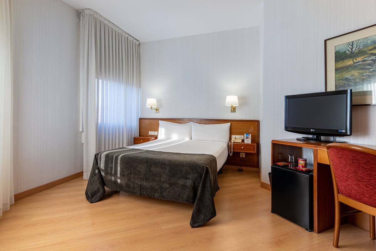 A hotel room with a bed, a TV, a desk, and a chair.