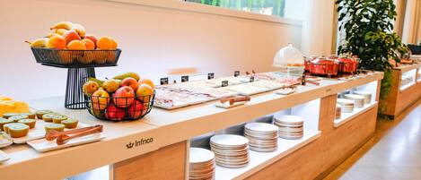 Una mesa de buffet con diversas frutas, una presentación de alimentos y platos apilados cuidadosamente.