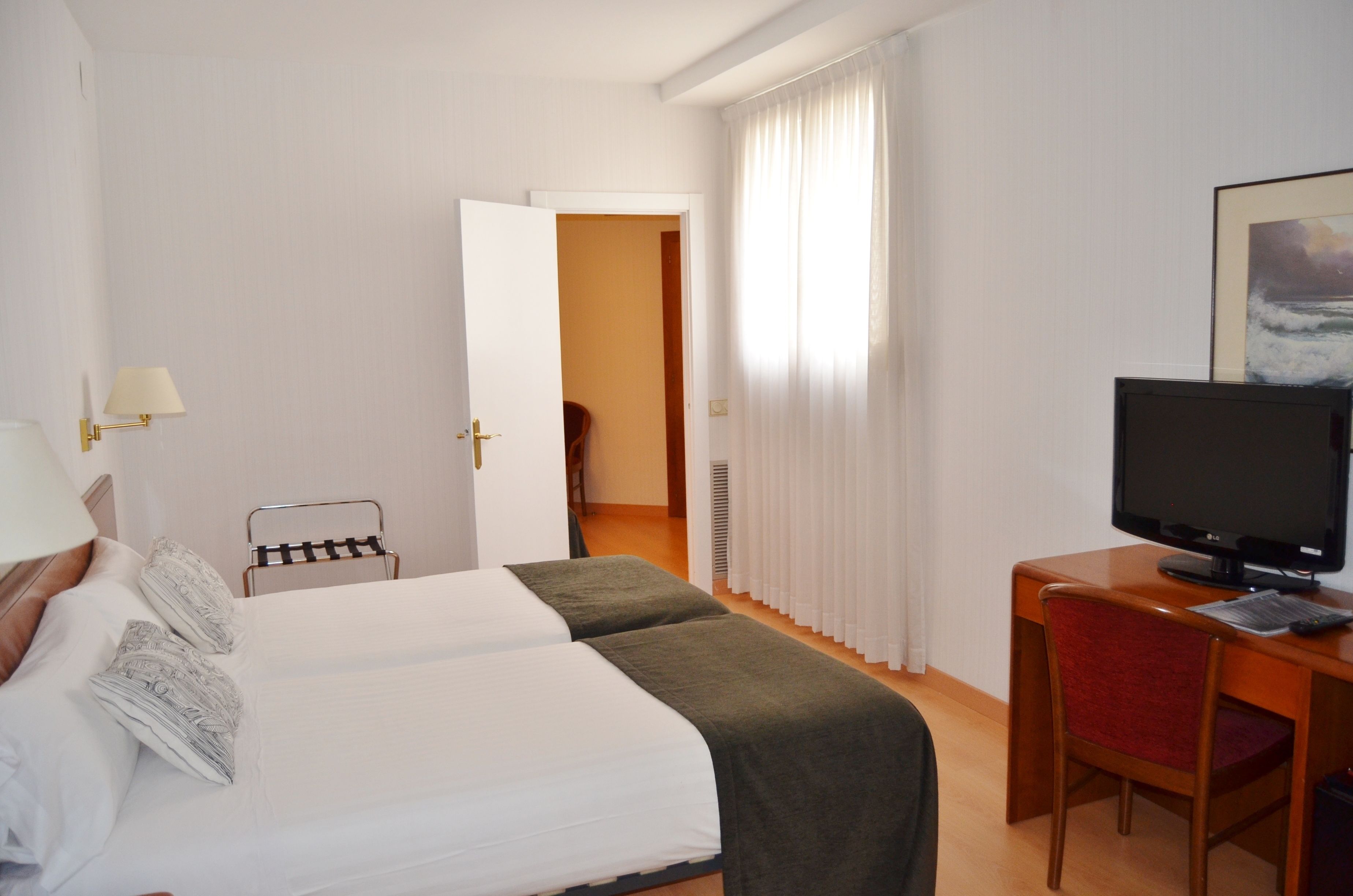 Habitación de hotel con dos camas, un escritorio con televisor y una silla.