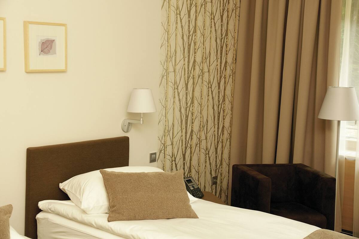A hotel room with a bed, two wall-mounted lamps, a chair, and a curtain with a tree pattern.