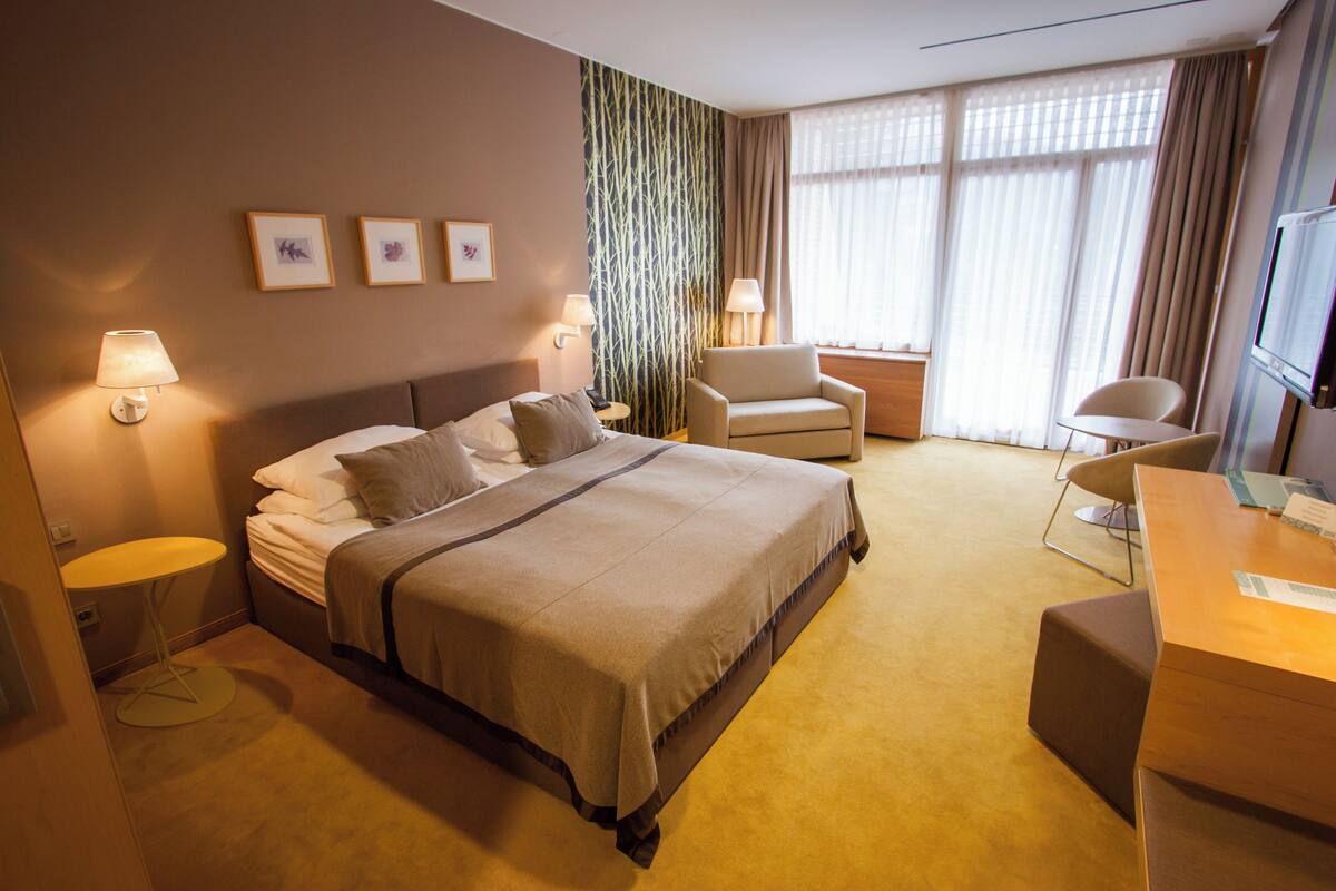 A hotel room with a bed, two bedside tables, a desk, a chair, and a TV.