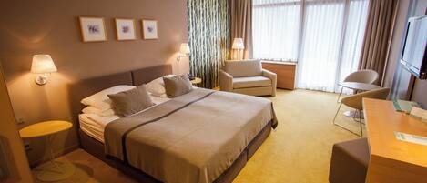A hotel room with a bed, two bedside tables, a desk, a chair, and a TV.