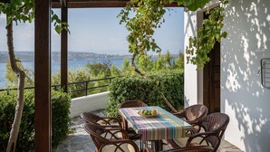 Un patio al aire libre con mobiliario de mimbre, una mesa con mantel a rayas y vistas al mar.