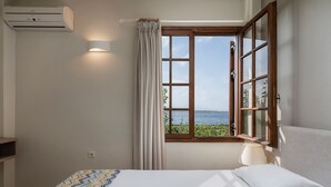 Un dormitorio con un ventanal grande, una cama, una lámpara de noche y un aire acondicionado instalado en la pared.