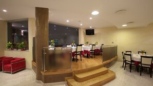 A modern restaurant with a wooden staircase, red seating, and large windows.