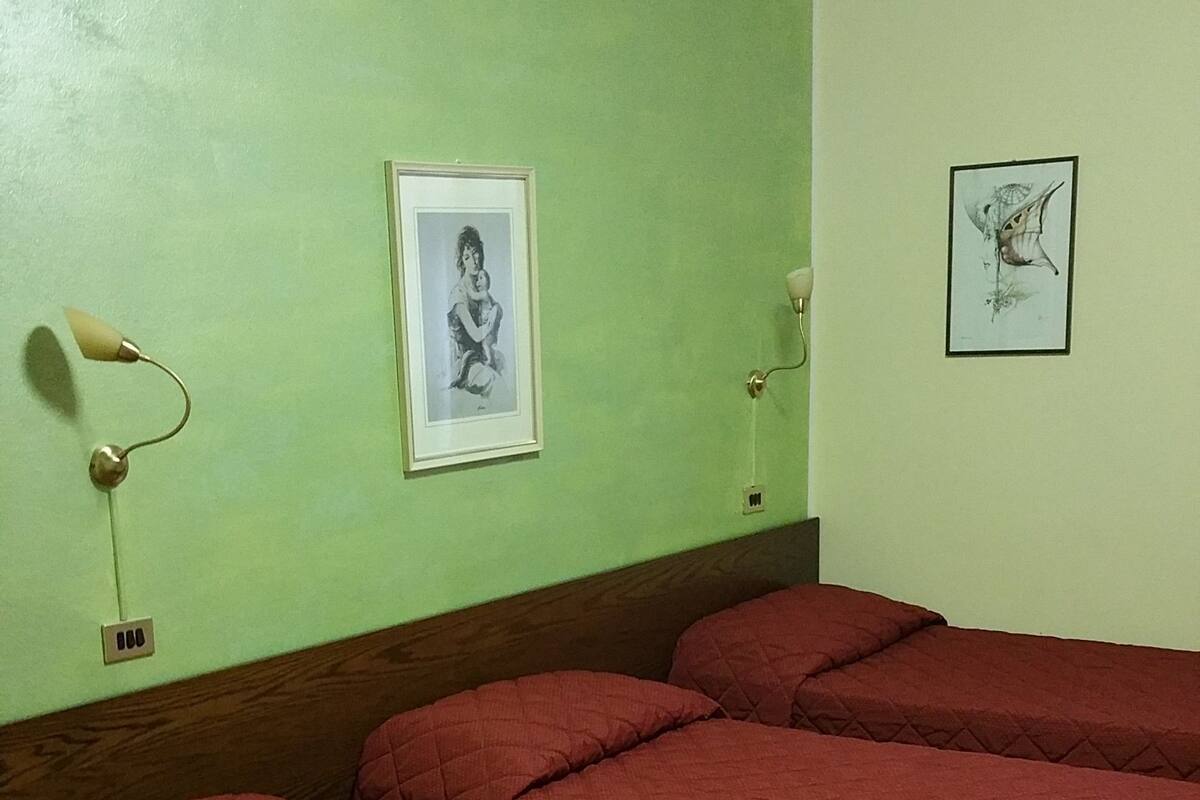 Ein Zimmer mit grüner Wand, einem Bett mit roter Bettwäsche und zwei gerahmten Bildern.