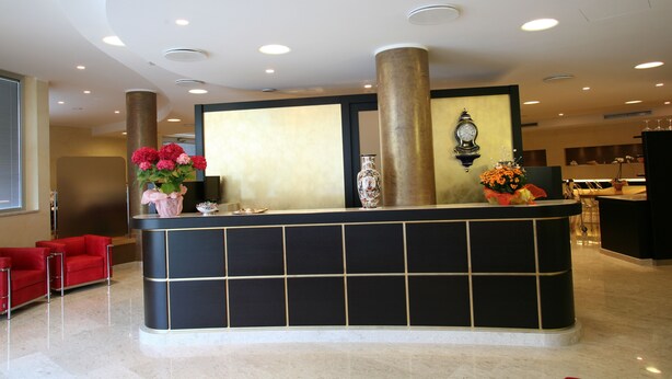 A reception desk with a black and gold design, a large vase with flowers, and a clock on the wall.