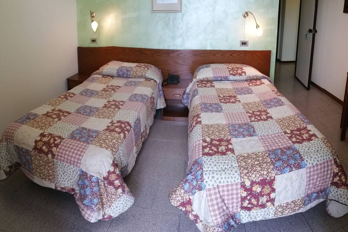 Ein Zimmer mit zwei Betten, jedes mit einer floralen Stegdecke, einem Holz-Kopfteil und jeweils zwei Wandleuchten.