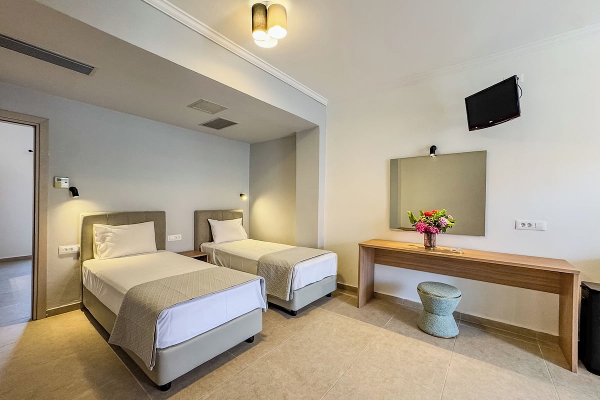 A hotel room with two beds, a small table with a vase of flowers, a television mounted on the wall, and a door.