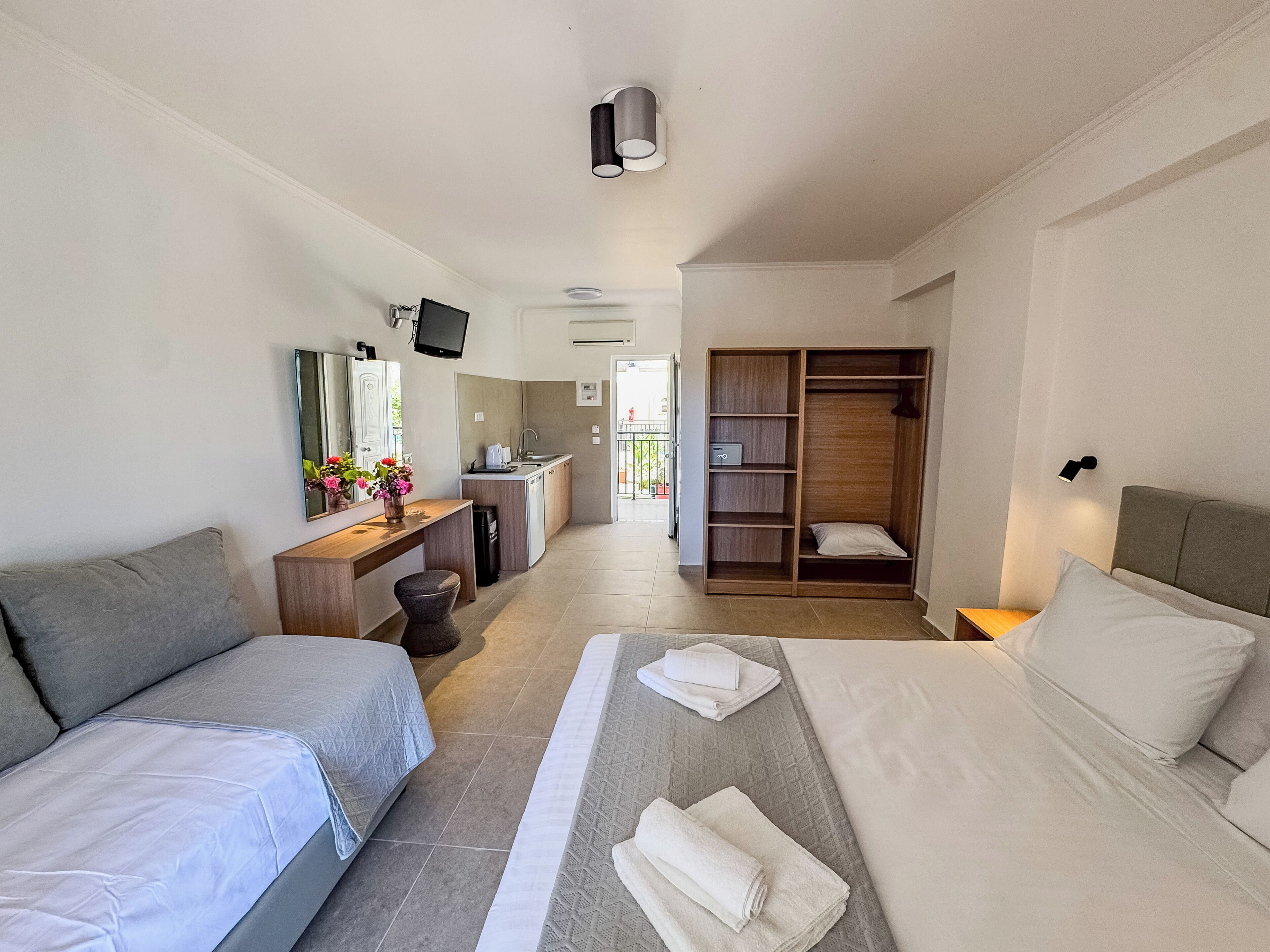 A hotel room with two beds, a desk with a computer, a wardrobe, and a bathroom visible in the background.