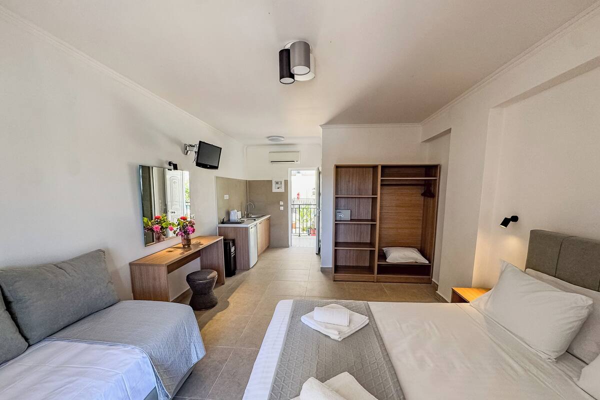 A hotel room with two beds, a desk with a computer, a wardrobe, and a bathroom visible in the background.