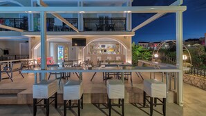 A multi-level outdoor dining area with tables and chairs, a bar area, and a balcony with a railing. - Athina Apts (Zakynthos)