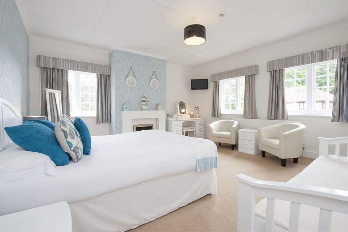 A spacious bedroom with a large bed, a desk, two chairs, a television, and a fireplace.