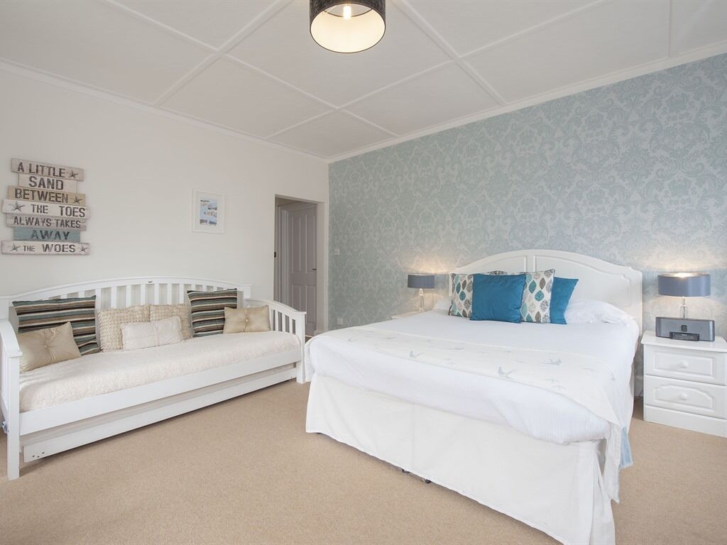A bedroom with a white bed, a white sofa, and a nightstand with a lamp.