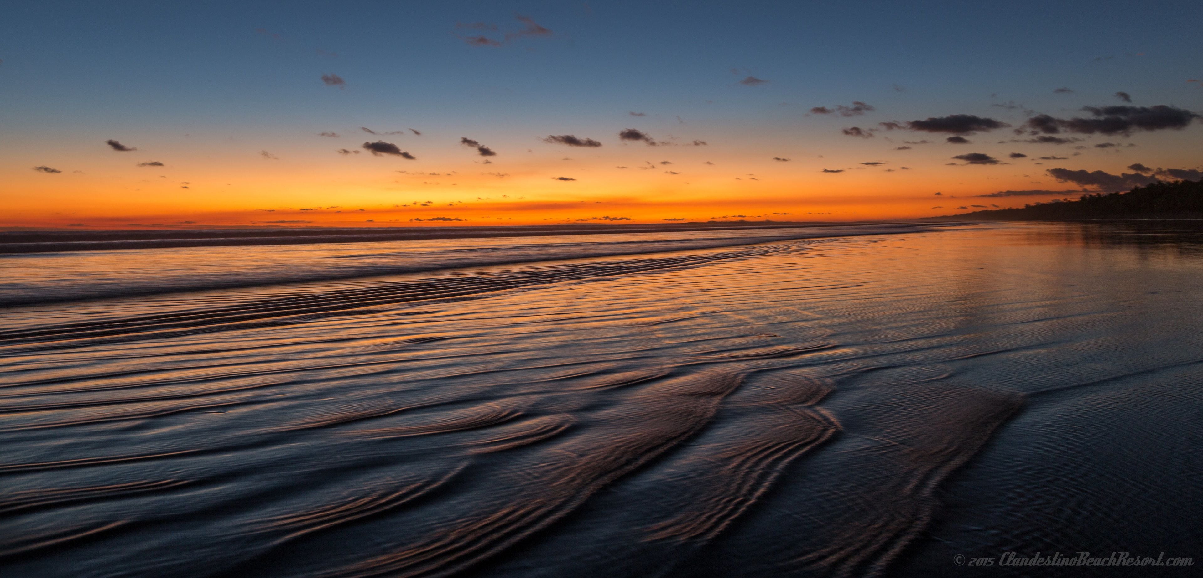 A beach at sunset with calm waves and a clear sky.