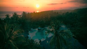 Un resort tropicale con piscina, circondato da palme e vista sul tramonto.