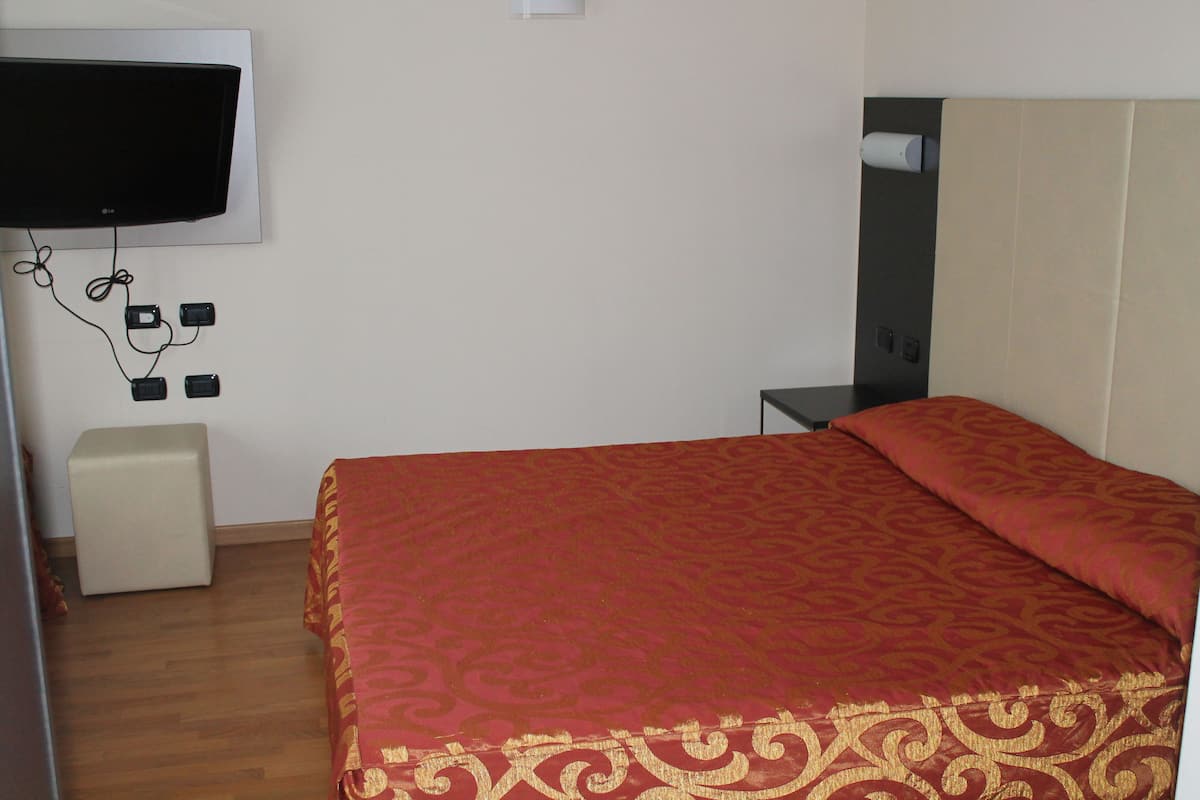 Hotellihuone, jossa on sänky, seinälle asennettu televisio ja pieni yöpöytä.