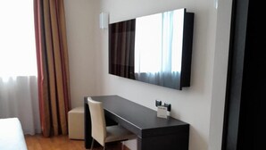 A hotel room with a bed, a desk, a chair, a flat-screen TV, and a window with curtains. - Raya Hotel Motel (Mediglia)