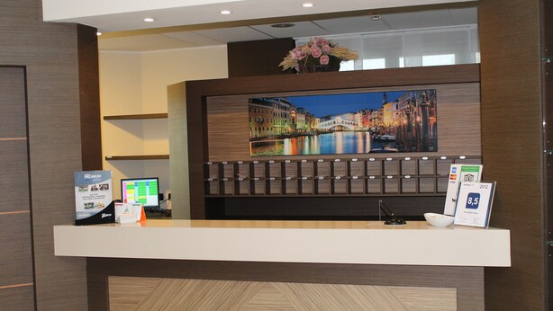A hotel reception desk with a large framed picture of a cityscape, a computer, and a sign indicating a 8.5-star rating. - Raya Hotel Motel (Mediglia)