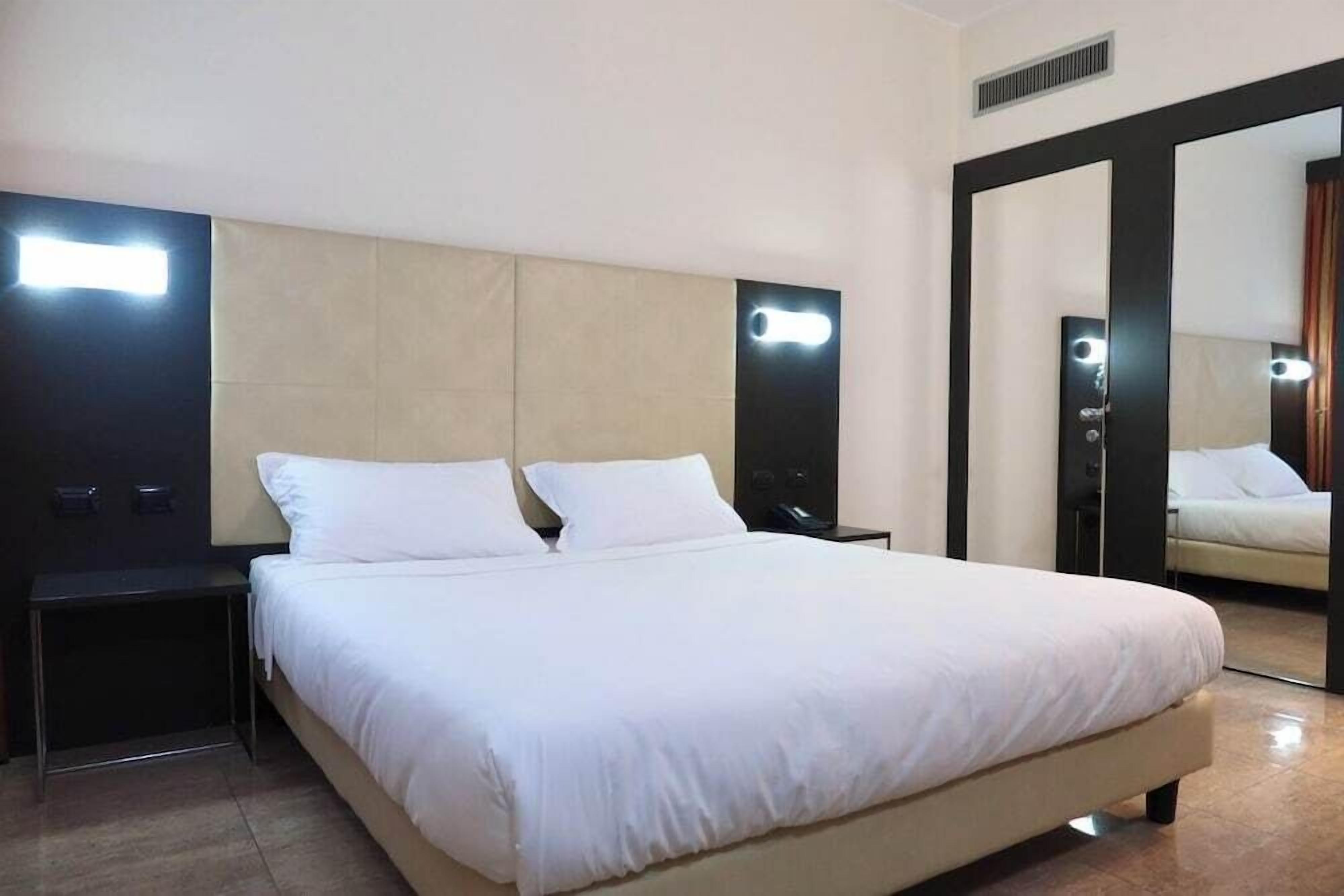 Una habitación de hotel con una cama grande, dos mesitas de noche, un espejo y un armario.