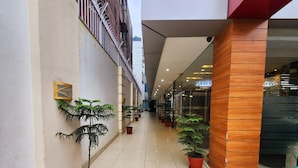 A corridor with potted plants, a wooden column, and a glass door leading to a room. - Hotel Lee International (Kolkata)