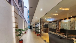 A hotel corridor with potted plants, a reception area with patterned decor, and a modern ceiling design. - Hotel Lee International (Kolkata)