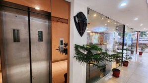 An interior with a reception desk, a digital elevator display, and potted plants. - Hotel Lee International (Kolkata)