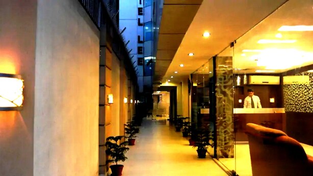A hotel corridor with a reception desk, potted plants, and a staircase leading to an upper level. - Hotel Lee International (Kolkata)