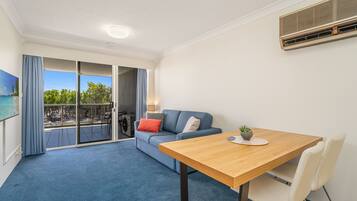 A modern living room with a blue carpet, a wooden table, a sofa with cushions, and a sliding glass door leading to an outdoor area.