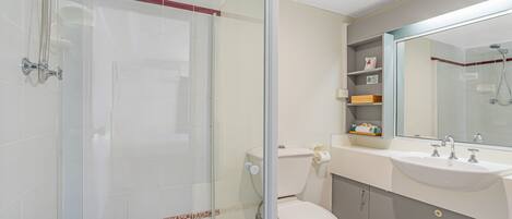 Un baño moderno con cabina de ducha de vidrio, inodoro, lavabo con espejo y repisa con artículos de aseo.