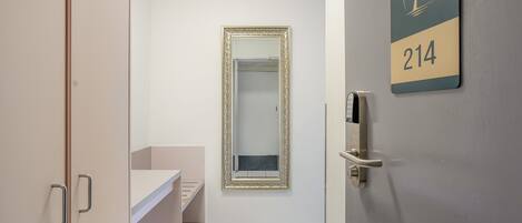 A hotel room with a bathroom, a door with a number sign, and a mirror.
