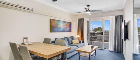 A modern hotel room with a dining area, a sofa, a coffee table, and a ceiling fan.