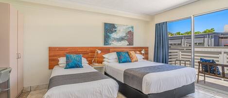 A hotel room with two beds, a wooden headboard, a painting, and a balcony with a view.