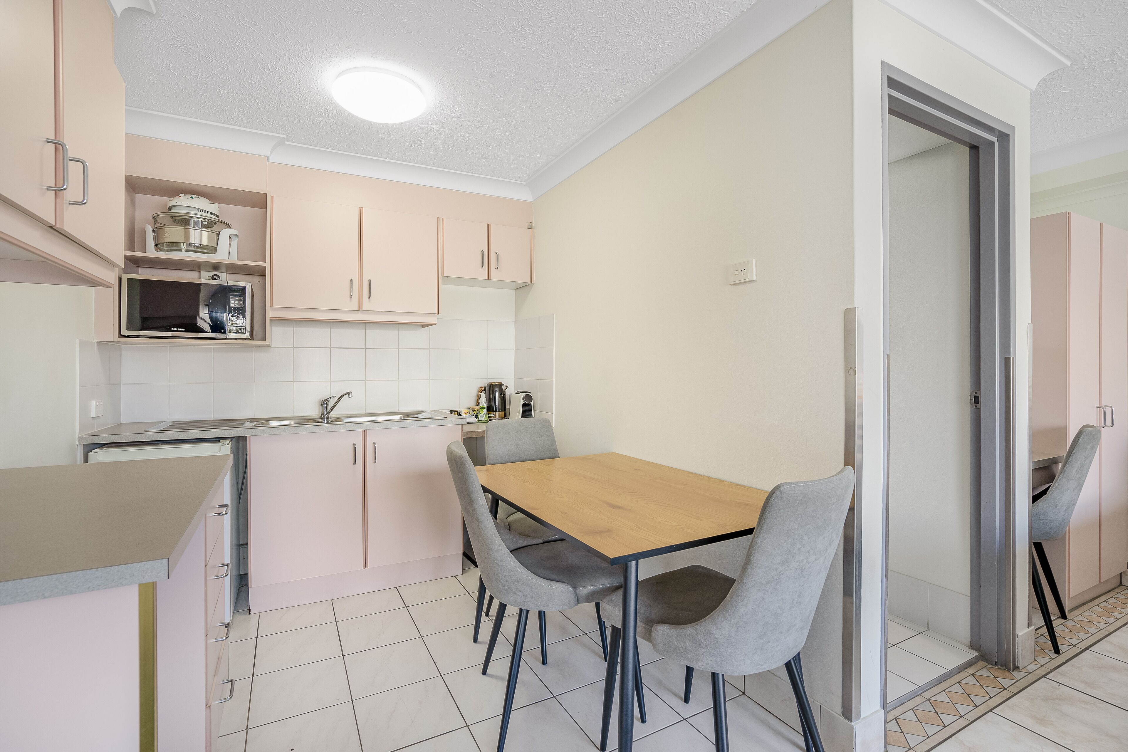 Una cocina compacta con comedor, que incluye una mesa de madera y sillas grises, un microondas y una tetera sobre la encimera.