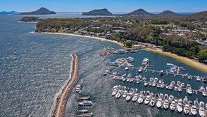 An aerial view of a coastal marina with boats docked, surrounded by residential buildings and natural landscapes. - Nelson Towers Motel & Apartments (Nelson Bay)