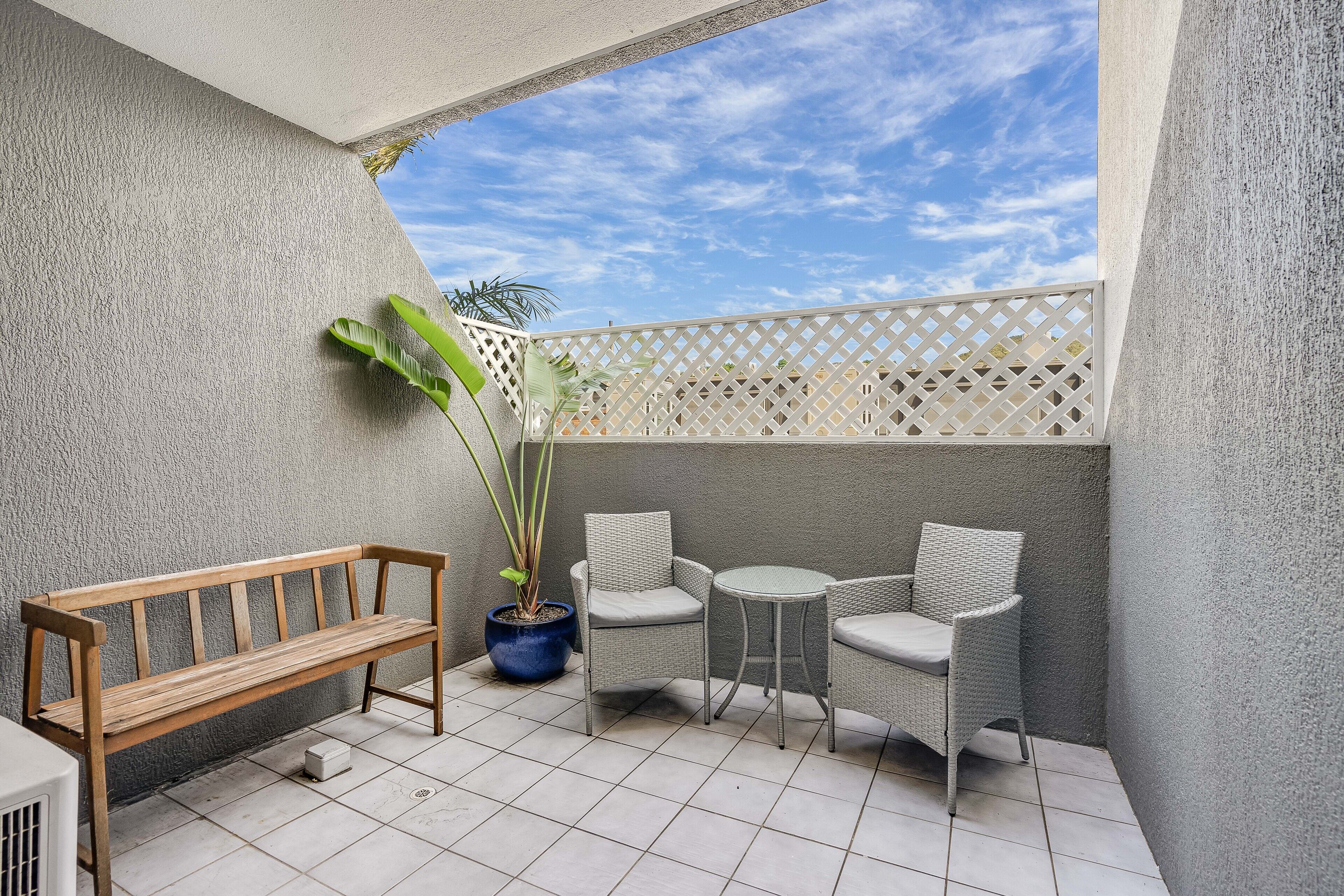 A balcony with a wooden bench, wicker chairs, and a potted plant.