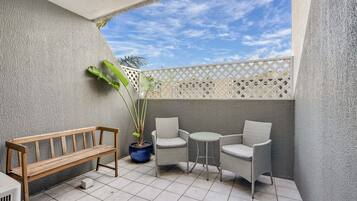 A balcony with a wooden bench, wicker chairs, and a potted plant.