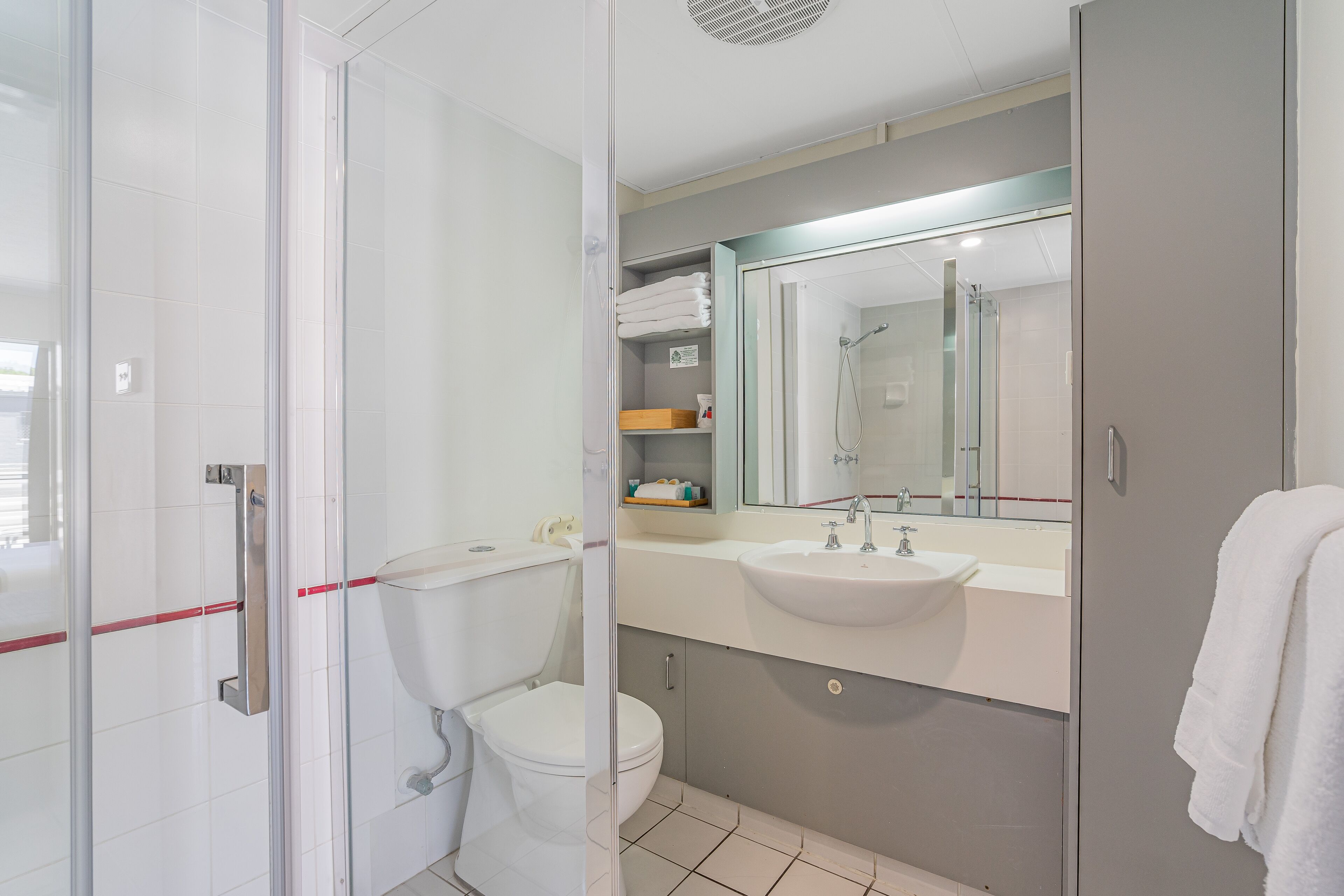 Un baño moderno con cabina de ducha de vidrio, inodoro blanco, lavabo con espejo y toalla colgada en la pared.