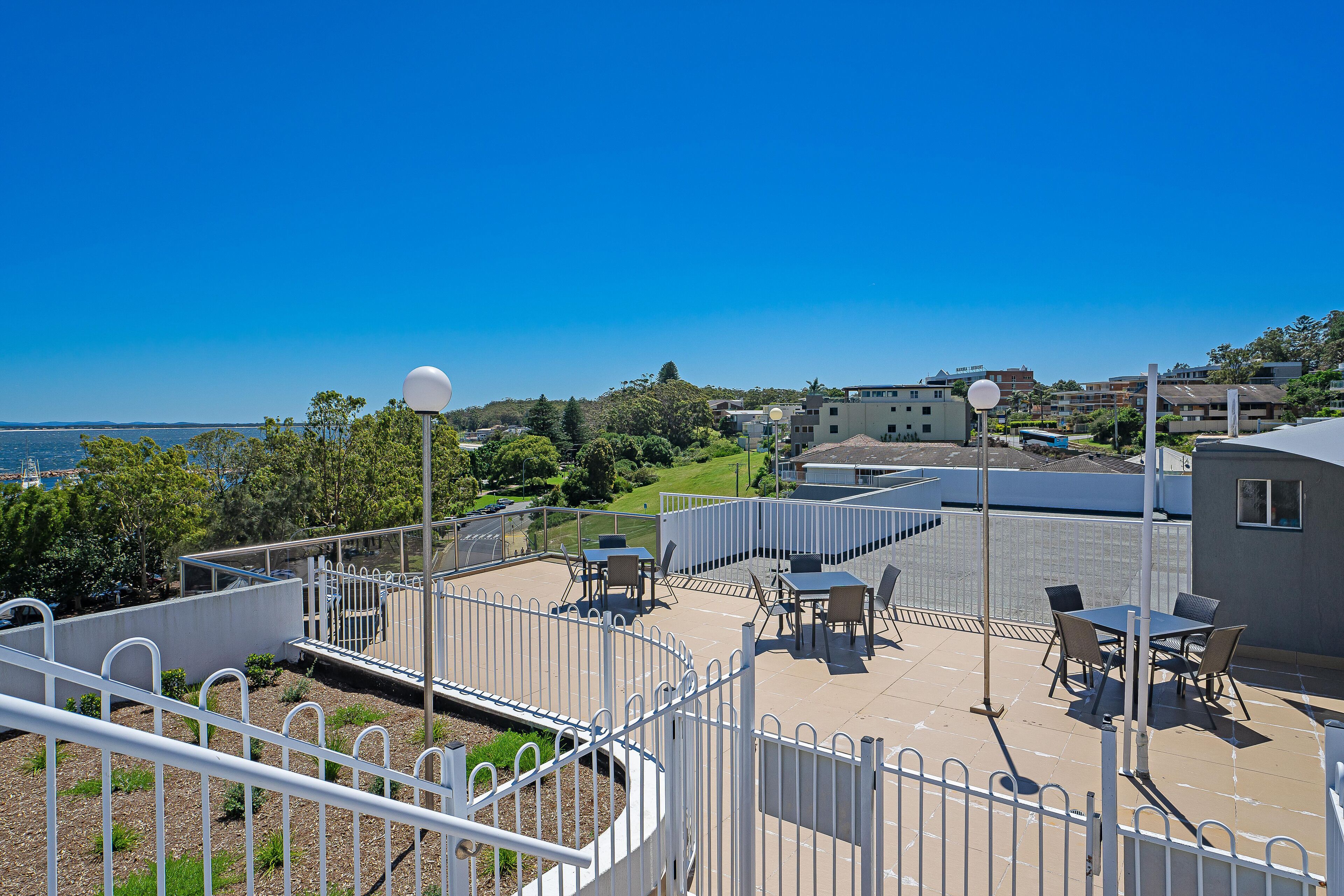 A rooftop patio with outdoor seating, a view of the sea, and a white fence.